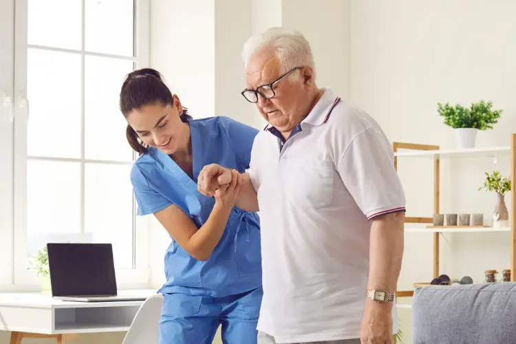 Nurse assists elderly man in walking inside a bright, modern living room with a window and shelves.