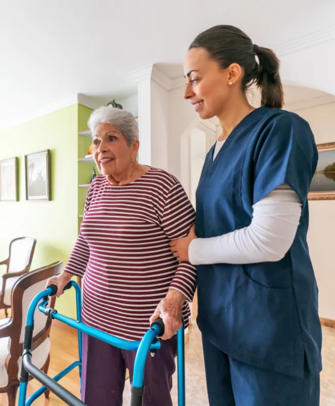 A nurse assists an elderly woman using a walker in a home setting.