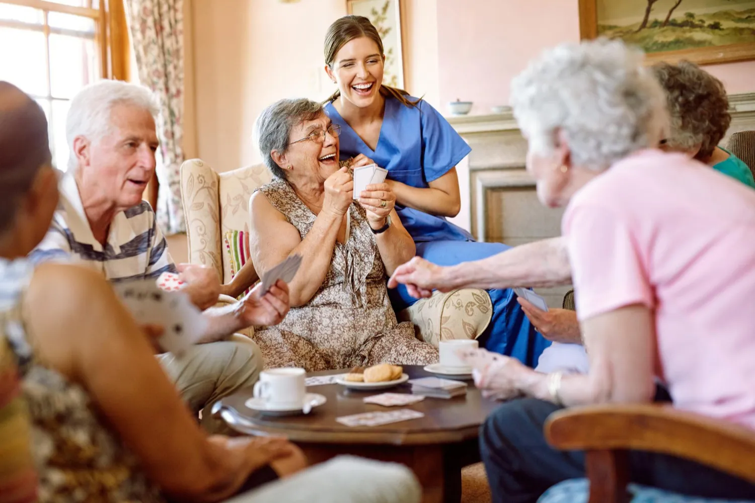 b2 A group of seniors and a caregiver smile and laugh together while playing cards around a table.