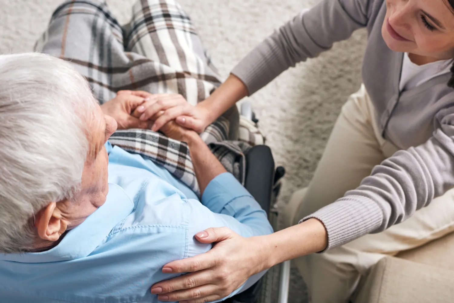 b4 Elderly person in a wheelchair holding hands with a caregiver, both smiling and sharing a warm moment.