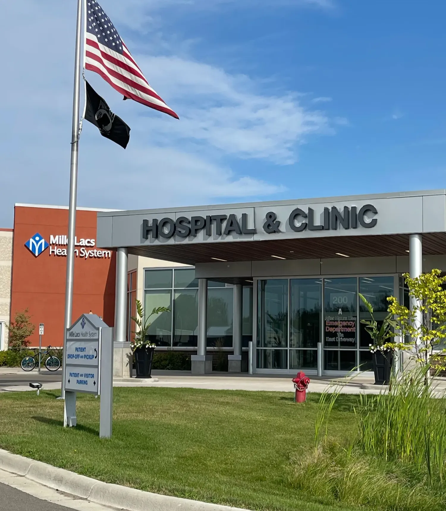 Hospital & Clinic entrance with American flag, blue sky, and nearby healthcare system sign outside building.