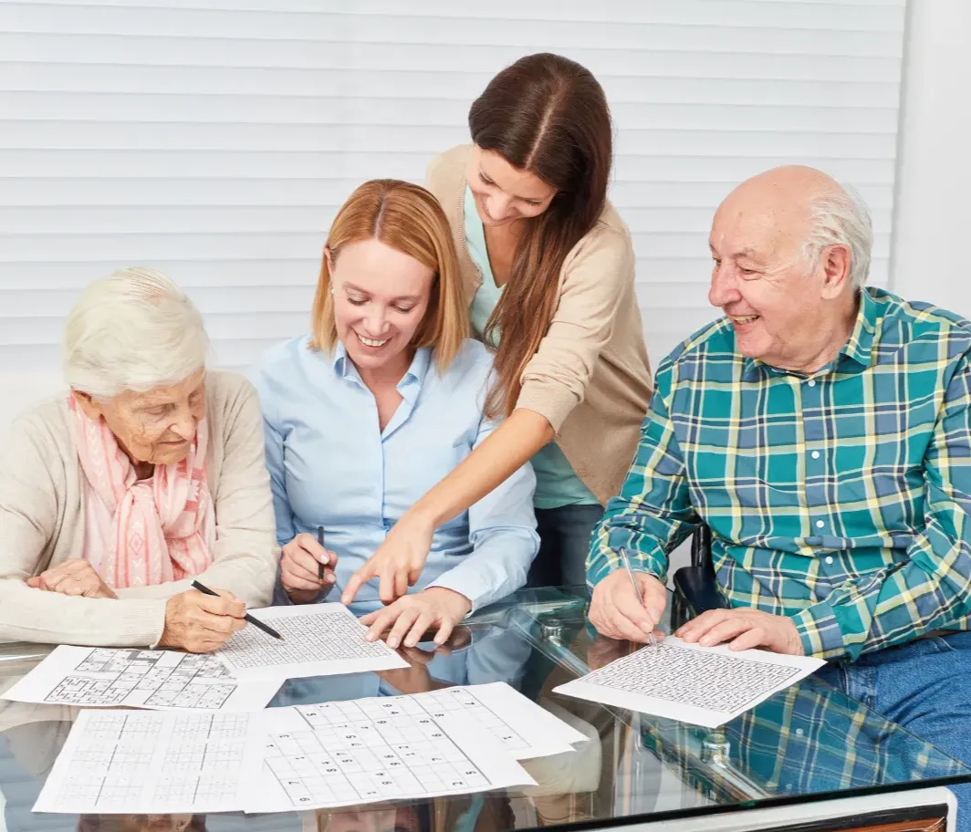 Four people sit at a table solving puzzles together, smiling and enjoying each other’s company.