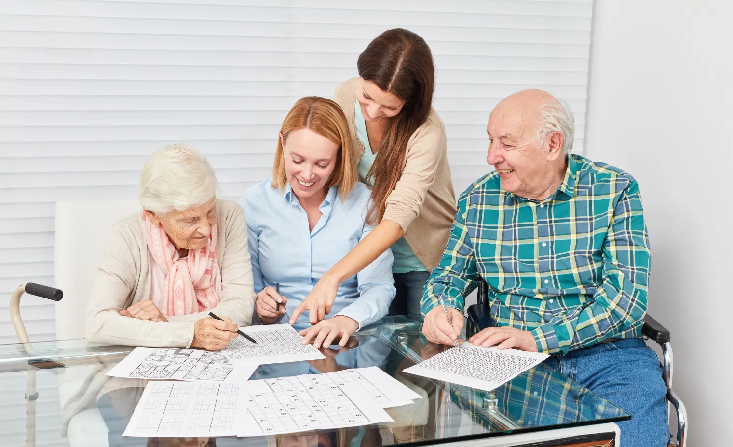 Four people, including two seniors, sit at a table solving puzzles together and smiling.