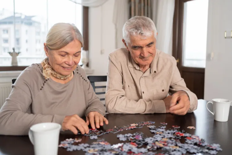 Two older adults sit at a table, smiling and assembling a jigsaw puzzle together.